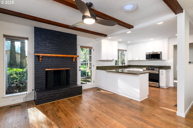 kitchen with stainless steel appliances, white cabinetry, beam ceiling, and kitchen peninsula