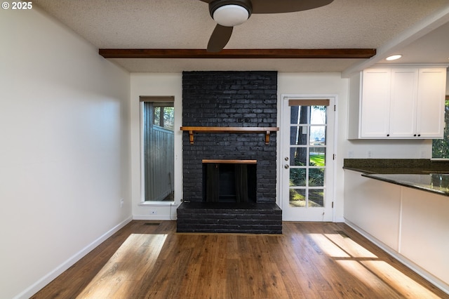 unfurnished living room with hardwood / wood-style flooring, beam ceiling, a brick fireplace, and a textured ceiling