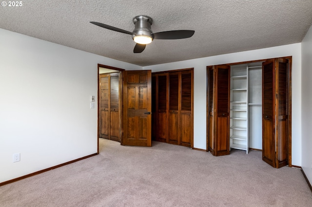 unfurnished bedroom with multiple closets, ceiling fan, light carpet, and a textured ceiling