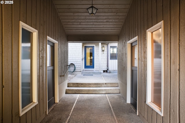 hall with wood ceiling, lofted ceiling, and wood walls