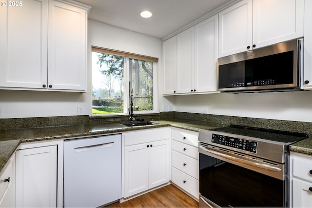 kitchen with stainless steel appliances, dark stone countertops, white cabinets, and light wood-type flooring