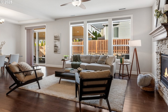 living room featuring ceiling fan, dark hardwood / wood-style flooring, and a stone fireplace