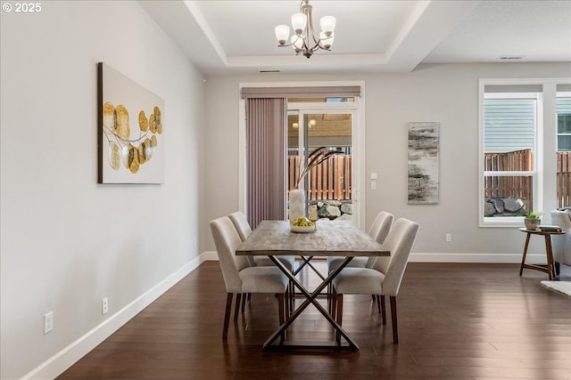 dining room with dark wood-type flooring, a chandelier, and a tray ceiling