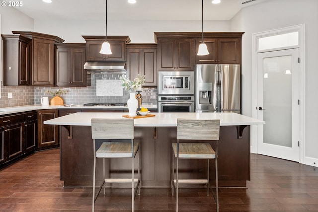 kitchen with appliances with stainless steel finishes, hanging light fixtures, a kitchen bar, and a kitchen island