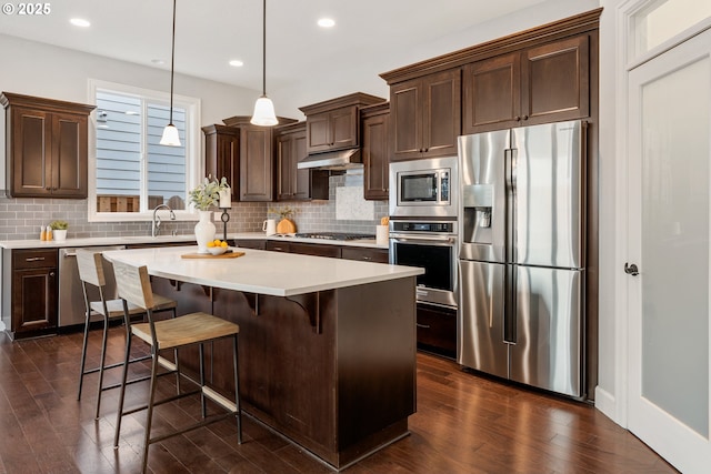 kitchen featuring pendant lighting, a center island, stainless steel appliances, dark hardwood / wood-style flooring, and dark brown cabinets