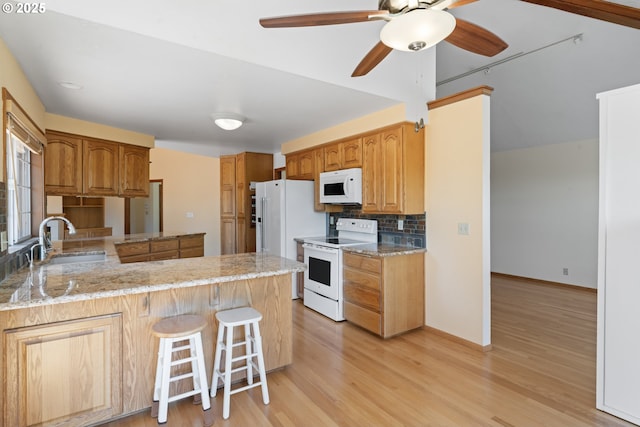 kitchen featuring a peninsula, white appliances, light wood-style floors, a sink, and backsplash