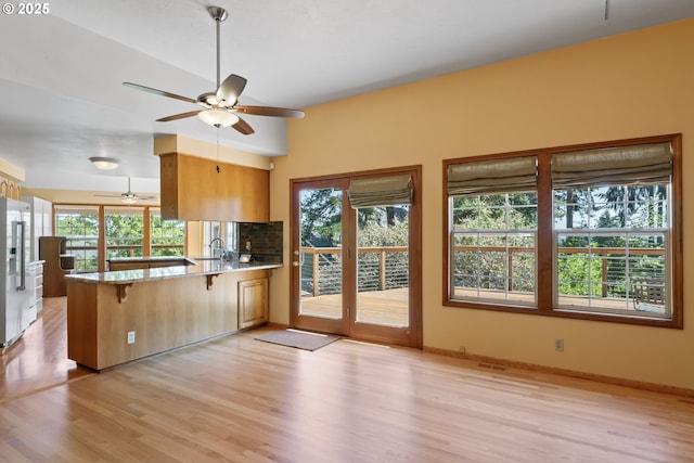 kitchen with a sink, a kitchen breakfast bar, light wood-style flooring, a peninsula, and a ceiling fan