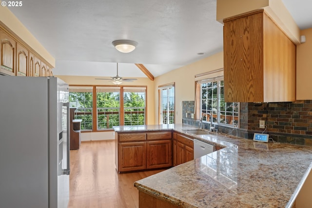 kitchen featuring tasteful backsplash, a sink, a peninsula, white appliances, and light wood-style flooring