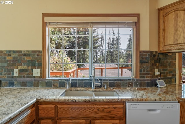 kitchen with light stone counters, a sink, dishwasher, and tasteful backsplash