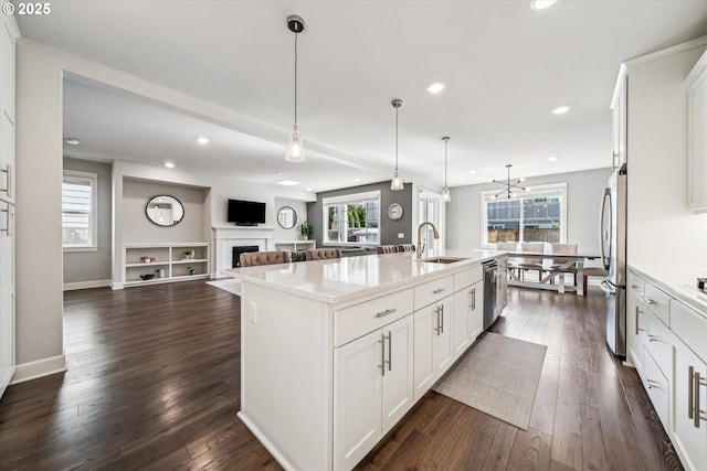 kitchen with dark wood-type flooring, a fireplace, a sink, appliances with stainless steel finishes, and an island with sink