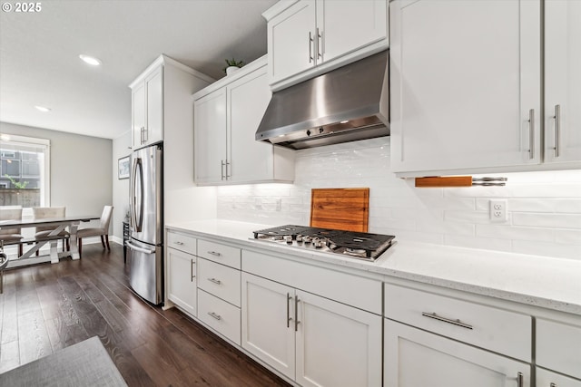 kitchen with under cabinet range hood, stainless steel appliances, white cabinetry, tasteful backsplash, and dark wood finished floors