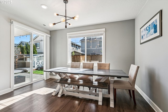 dining space with dark wood-type flooring, a wealth of natural light, and a notable chandelier