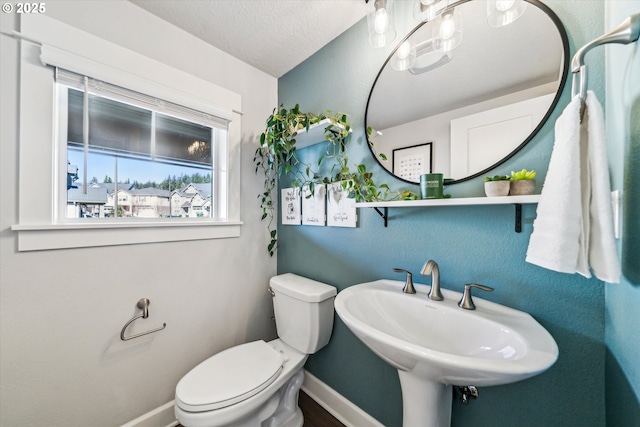 half bath with toilet, a textured ceiling, baseboards, and a sink