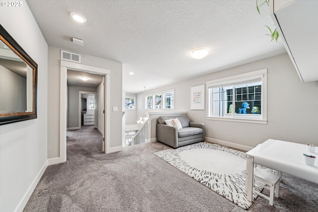 sitting room with carpet floors, visible vents, a textured ceiling, an upstairs landing, and baseboards