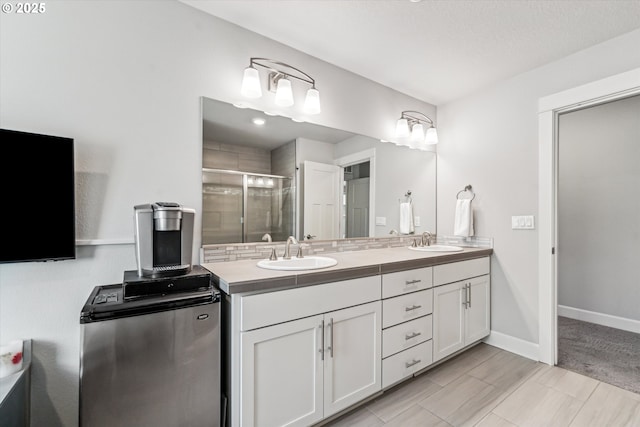 bathroom with double vanity, a shower stall, baseboards, and a sink