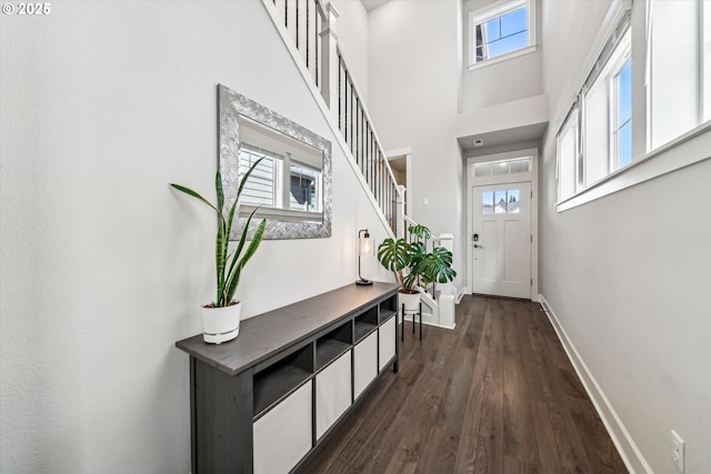 doorway with a towering ceiling, stairs, baseboards, and dark wood-type flooring