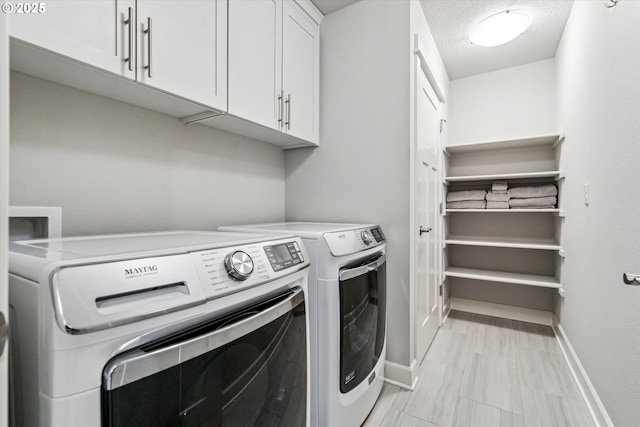 laundry room with baseboards, cabinet space, a textured ceiling, and washing machine and clothes dryer