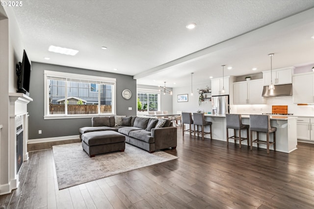 living room featuring a notable chandelier, a lit fireplace, dark wood finished floors, and a textured ceiling