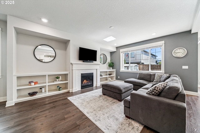 living area featuring dark wood-style floors, recessed lighting, a glass covered fireplace, a textured ceiling, and baseboards