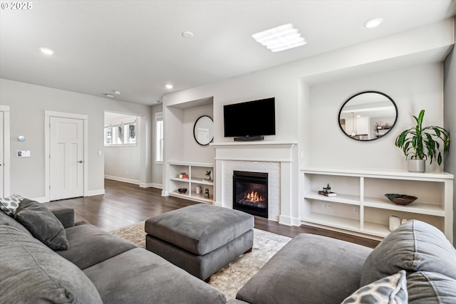 living area with baseboards, a glass covered fireplace, wood finished floors, and recessed lighting