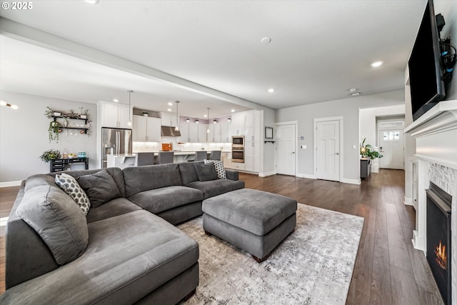 living room featuring a lit fireplace, baseboards, dark wood-style flooring, and recessed lighting