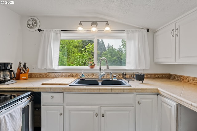 kitchen featuring a sink, white cabinetry, light countertops, a textured ceiling, and lofted ceiling