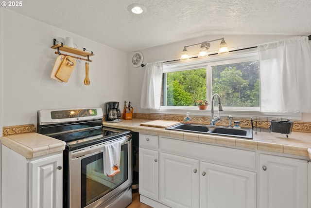 kitchen featuring electric range, a sink, a textured ceiling, white cabinets, and tile counters