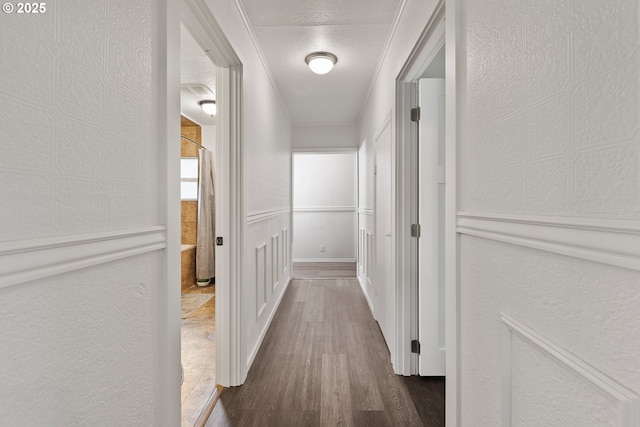 hallway featuring dark wood-type flooring, a textured wall, ornamental molding, and a textured ceiling