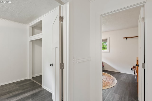 corridor featuring a textured ceiling, dark wood-style floors, ornamental molding, and baseboards