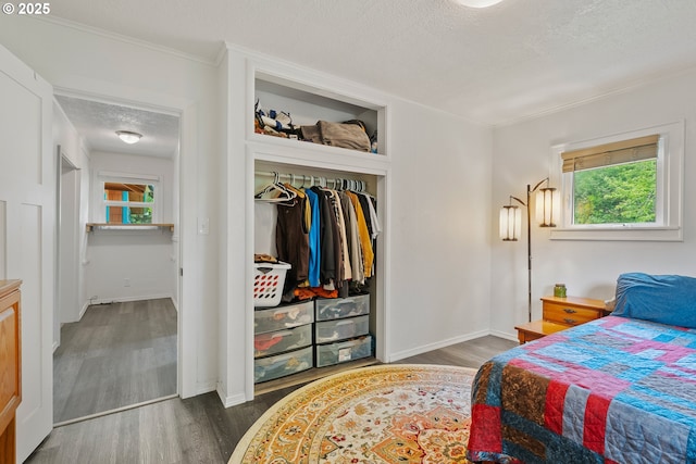 bedroom featuring wood finished floors, baseboards, a closet, a textured ceiling, and ornamental molding