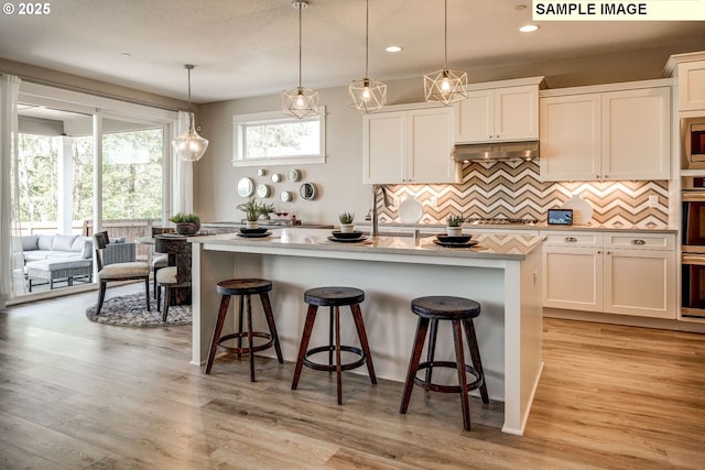 1124 N Helens View Dr, Ridgefield, WA 98642 - kitchen featuring a breakfast bar area, hanging light fixtures, white cabinets, an island with sink, and under cabinet range hood