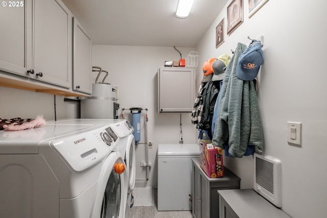 washroom with secured water heater, light hardwood / wood-style floors, cabinets, and washing machine and clothes dryer