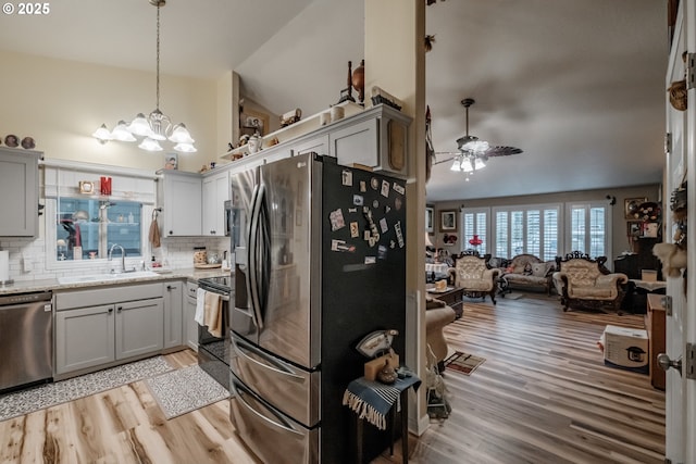 kitchen with lofted ceiling, ceiling fan with notable chandelier, gray cabinets, appliances with stainless steel finishes, and tasteful backsplash