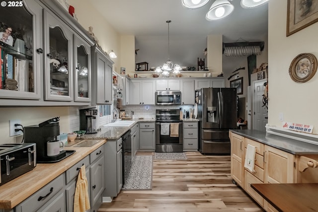 kitchen with pendant lighting, sink, gray cabinets, stainless steel appliances, and a chandelier