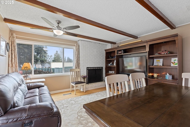 living room with a textured ceiling, beamed ceiling, ceiling fan, a fireplace, and light hardwood / wood-style floors