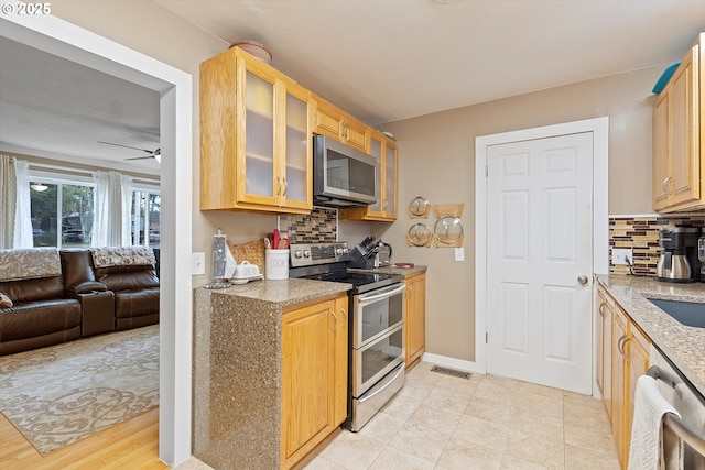 kitchen featuring appliances with stainless steel finishes, light brown cabinetry, ceiling fan, and decorative backsplash