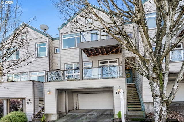 view of front of house featuring a garage, concrete driveway, a balcony, and stairs