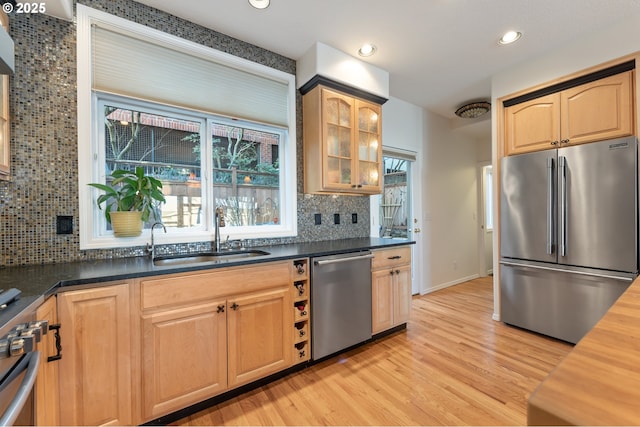 kitchen with a sink, appliances with stainless steel finishes, light wood-type flooring, decorative backsplash, and glass insert cabinets