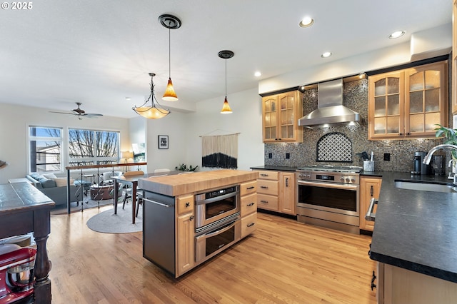 kitchen with dark countertops, wall chimney exhaust hood, a center island, stainless steel range oven, and a sink