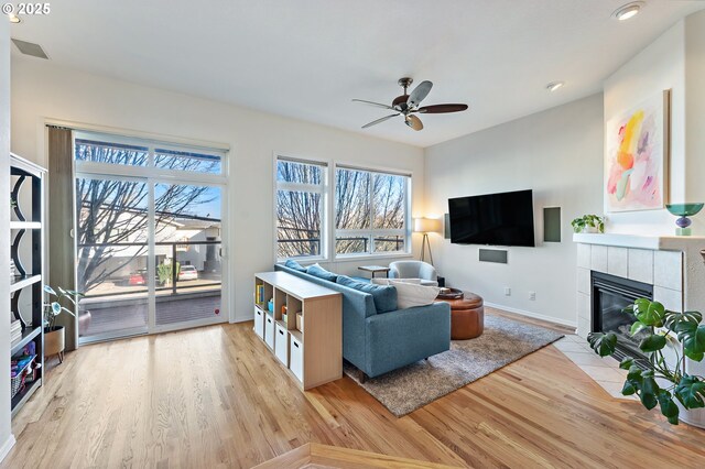 living room featuring ceiling fan, light hardwood / wood-style flooring, and a tiled fireplace