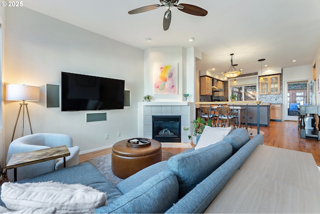 living area with a tile fireplace, recessed lighting, baseboards, and wood finished floors