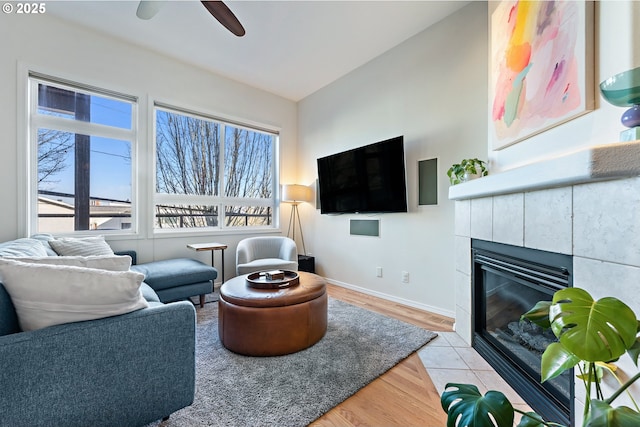 living area featuring baseboards, light wood-style floors, a tiled fireplace, and a healthy amount of sunlight