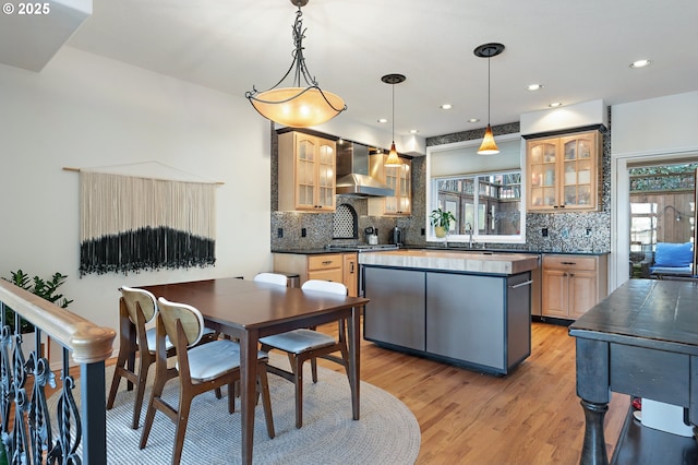 kitchen with wall chimney range hood, dark countertops, glass insert cabinets, and pendant lighting