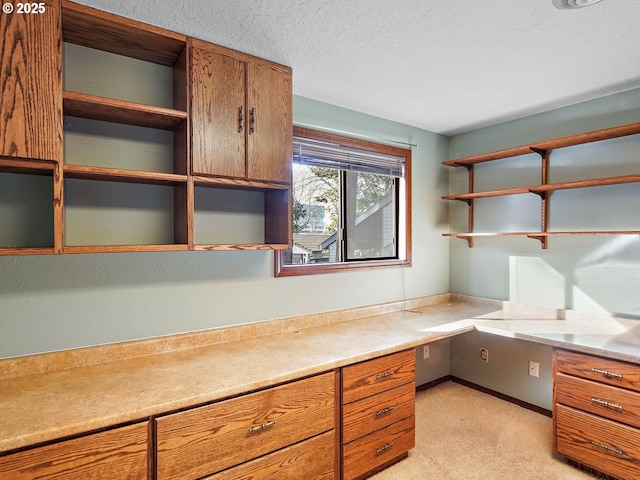 unfurnished office with light colored carpet, built in desk, and a textured ceiling