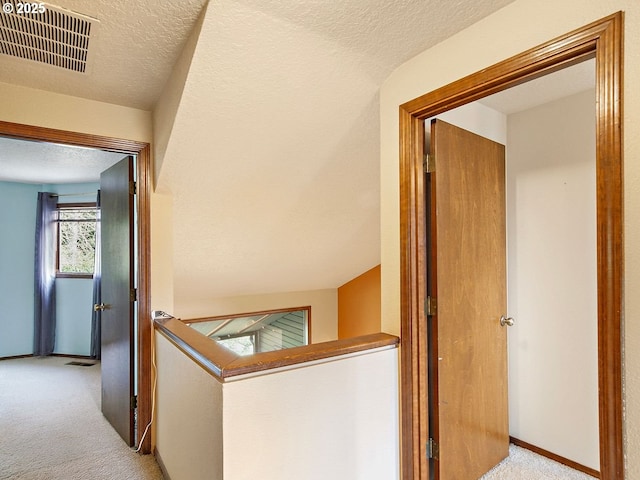 hall with light carpet and a textured ceiling