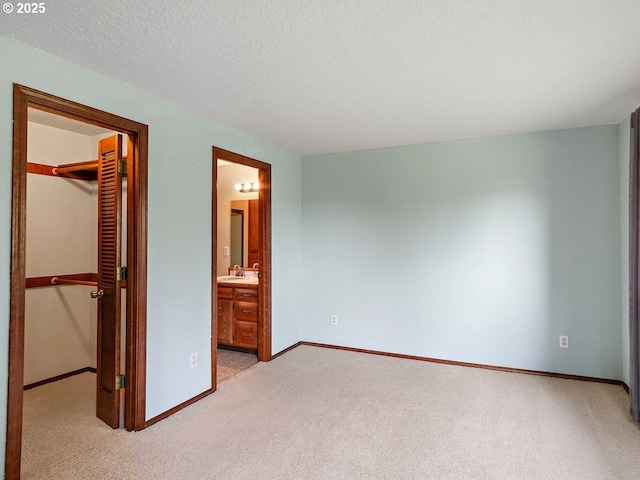 unfurnished bedroom with ensuite bathroom, a walk in closet, a textured ceiling, a closet, and light colored carpet