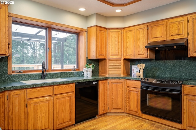 kitchen featuring dark countertops, under cabinet range hood, a sink, light wood finished floors, and black appliances