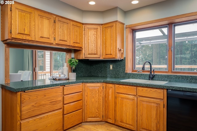 kitchen featuring brown cabinets, dishwasher, a sink, light wood finished floors, and a peninsula