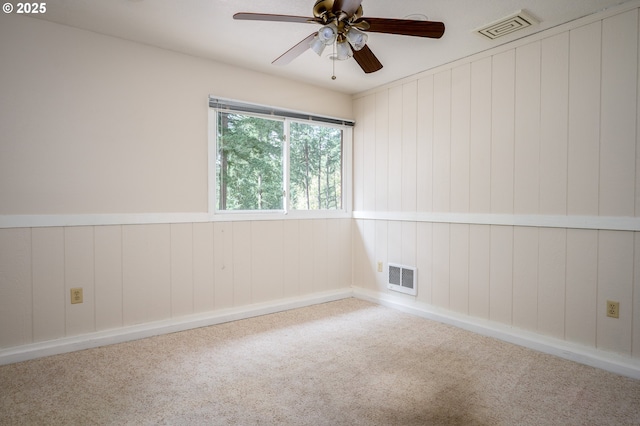 unfurnished room featuring visible vents, carpet flooring, a ceiling fan, and wooden walls