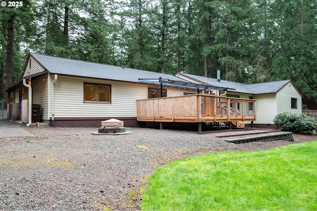 rear view of house featuring a wooden deck, a shingled roof, and an outdoor fire pit